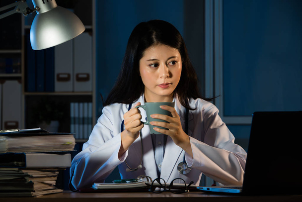 woman doctor working at night drinking coffee - Photo, Image