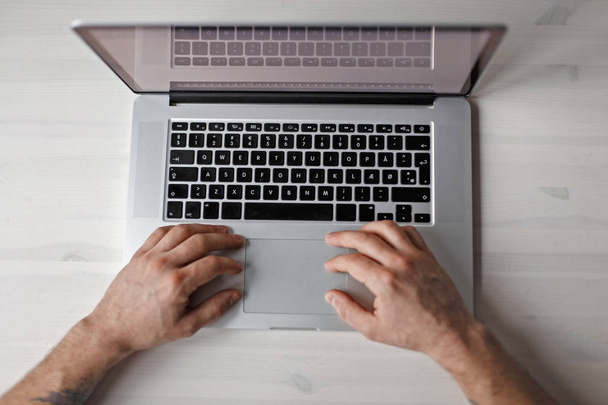 Erkek el ve metal bir dizüstü bilgisayarda Beyaz ahşap bir masa Üstten Görünüm - Fotoğraf, Görsel