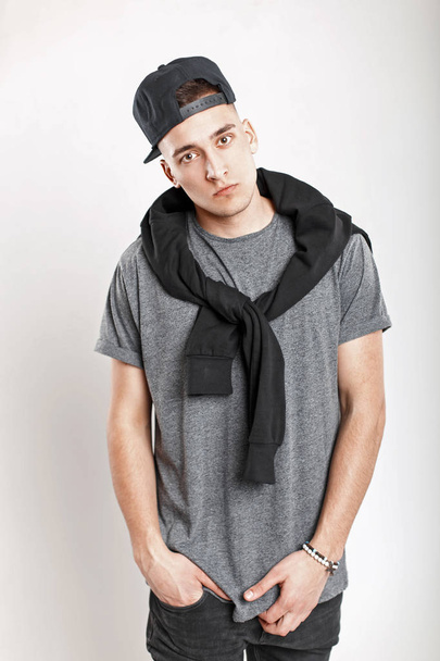 Stylish young man with a baseball cap in a gray t-shirt posing in the studio. - Fotó, kép