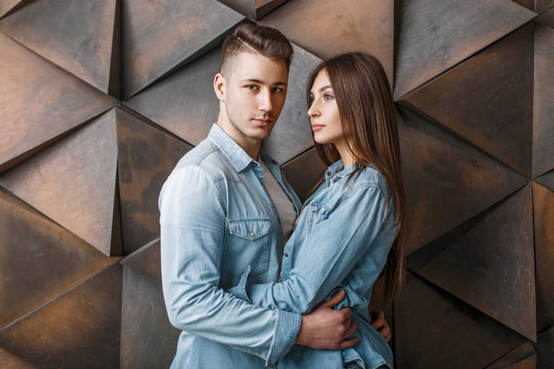 Красивая пара в модной джинсовой одежде обнимается у деревянной стены
 - Фото, изображение