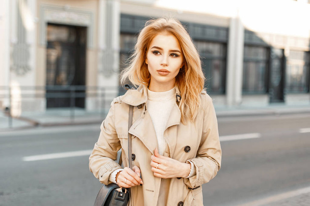Beautiful young slender girl in a light coat with a bag on the street - Photo, Image