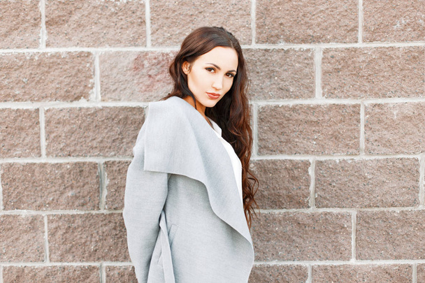 Hermosa chica en un abrigo gris de moda cerca de una pared de ladrillo
 - Foto, Imagen