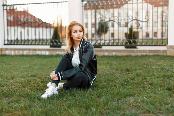 Belle étudiante dans une veste élégante et un jean noir avec des baskets blanches dans un collage sur l'herbe
 - Photo, image