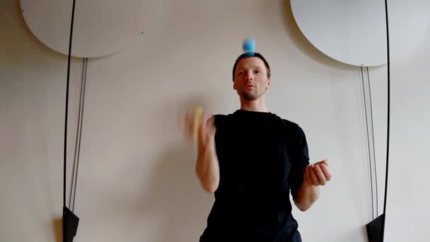 Jongleur met drie kleur ballen voor witte muur met decoratie aan zijden - Video