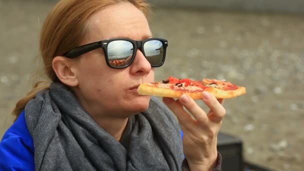 Een vrouw zit alleen op een verlaten strand bij slecht weer, kijkt naar de zee en eet pizza - Video