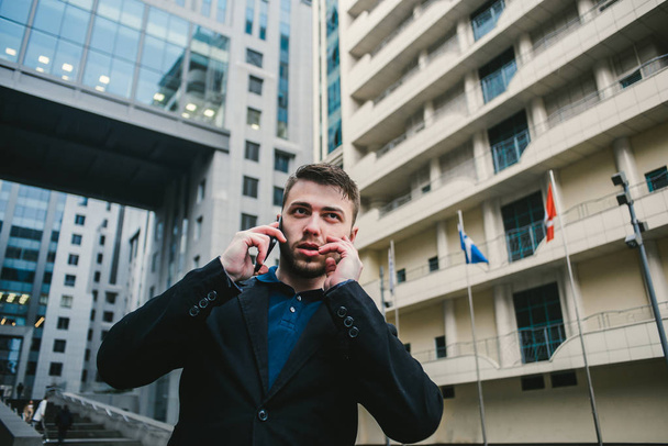 A young man with a beard businessman talking on the phone on the background of a modern business center. - Foto, immagini