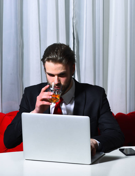 bearded man, businessman holding glass of whiskey works at laptop - Fotoğraf, Görsel