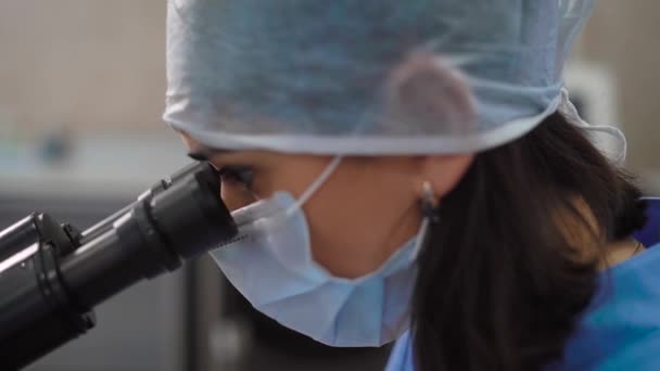 Close up shot of a female doctor on a face who examines under a microscope blood drops to detect diseases and confirm the healthy status of patients - Metraje, vídeo