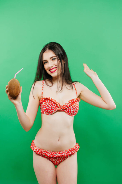 Portrait of Carefree Girl in Bright Swimsuit Posing with Cocktail in Studio on Green Background. - Фото, зображення