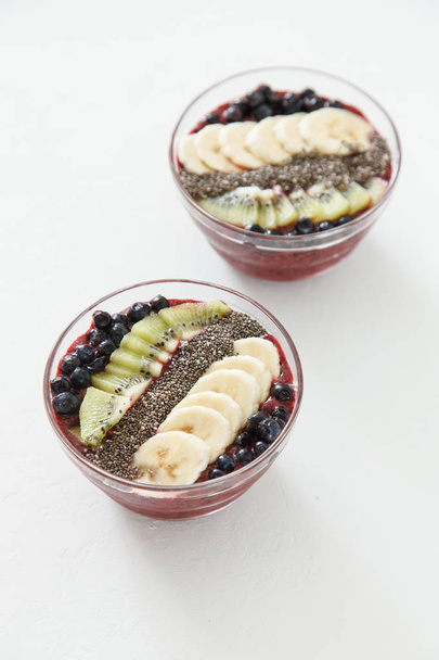 Twee platen van bessen smoothies met bosbessen, banaan en kiwi en chia zaden op een witte achtergrond. - Foto, afbeelding