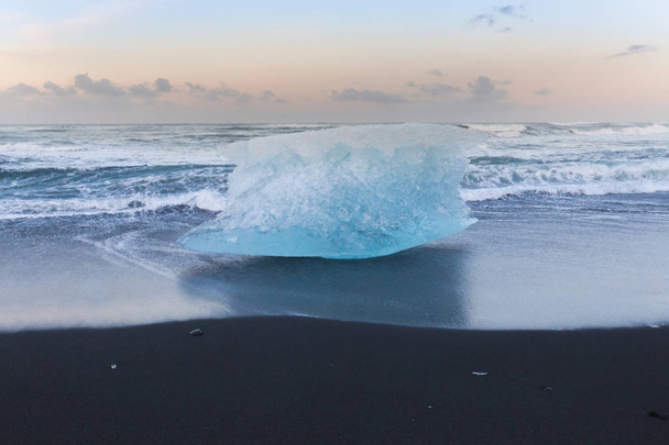 黒い砂のビーチ海のスカイラインを背景に壊れる氷 - 写真・画像