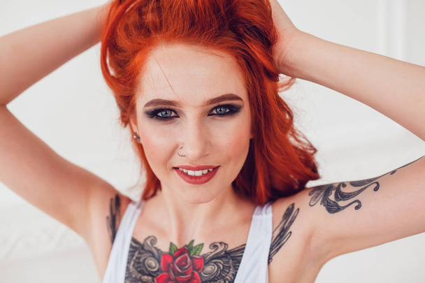 Portrait of a beautiful sexy girl with red hair and a tattoo. Woman with make-up and curls. - Foto, Imagem