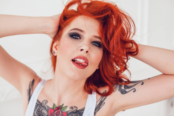 Portrait of a beautiful sexy girl with red hair and a tattoo. Woman with make-up and curls. - Zdjęcie, obraz
