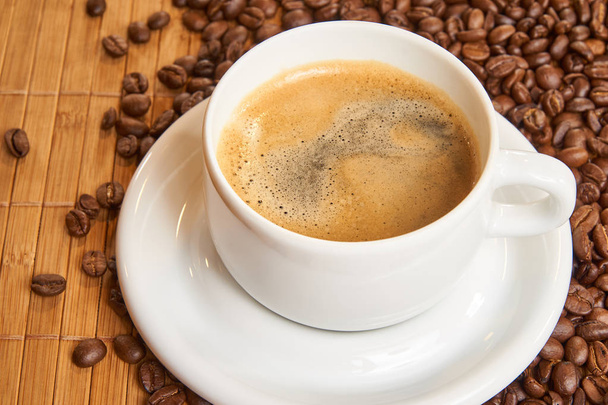 Fresh cup of coffee surrounded by coffee beans on a wooden background - Photo, Image