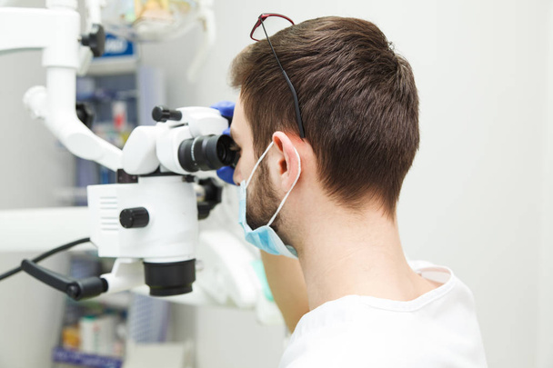 El dentista masculino está mirando a través de un microscopio
 - Foto, Imagen