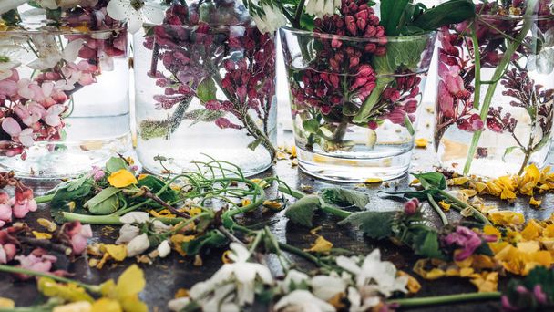 Picturesque bouquets of colorful spring flowers in glass vases bottles, standing in a row on a light wooden background table. - Foto, Imagen