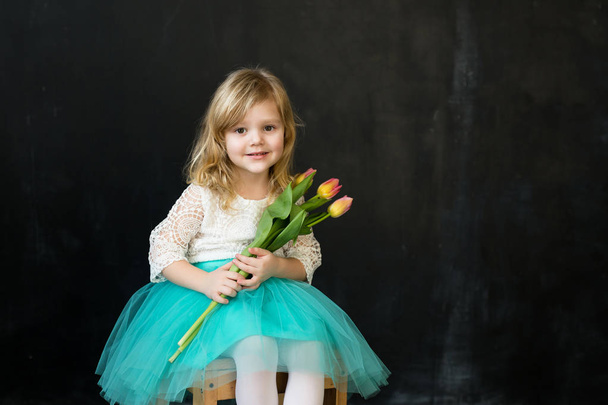 Mooi meisje met tulpen op een zwarte achtergrond - Foto, afbeelding