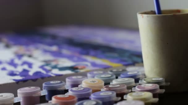 A menina desenha um quadro por números, mergulhando uma escova em um copo de água e um jarro de pintura. Colorir-Antistress
 - Filmagem, Vídeo