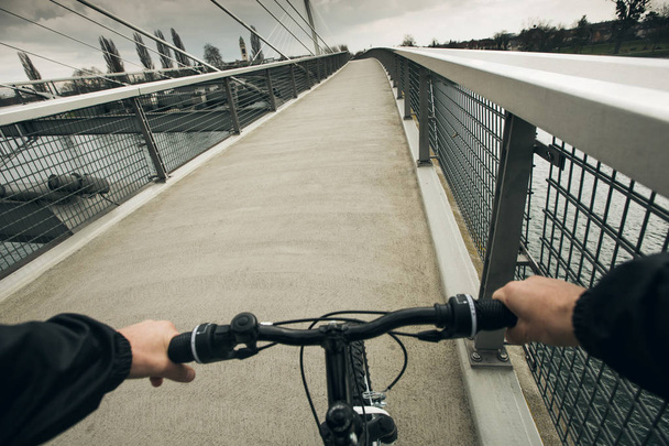 Close-up image of cyclist man hands on handlebar riding bike in park, face is not visible.Young man riding bike in city park over a bridge. - Фото, зображення