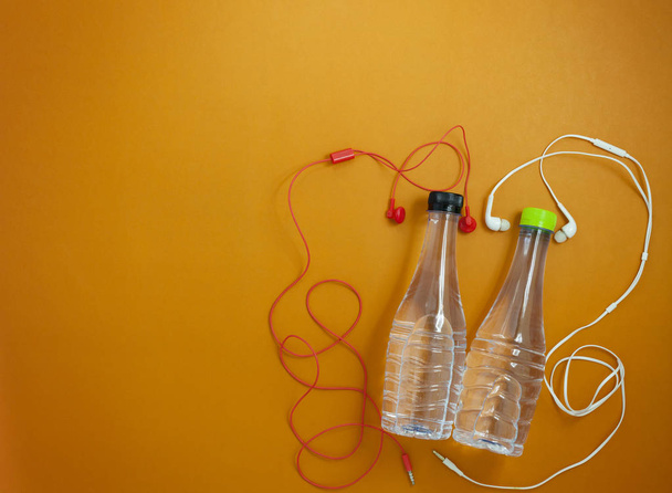 Nahaufnahme von Wasserflasche und Kopfhörer auf orangefarbenem Papier bac - Foto, Bild