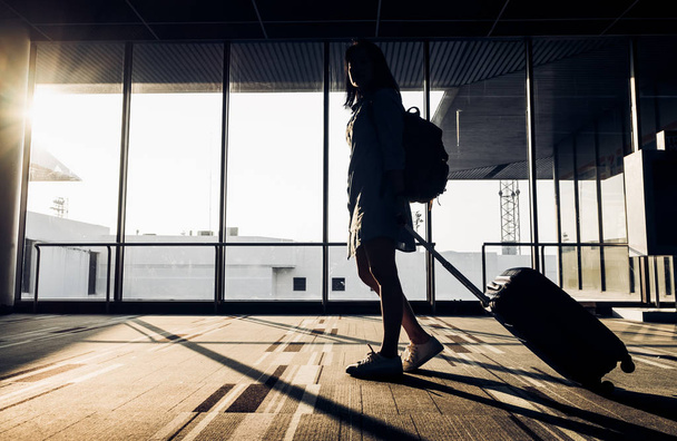 Silhouette of young girl walking with luggage walking at airport - Φωτογραφία, εικόνα