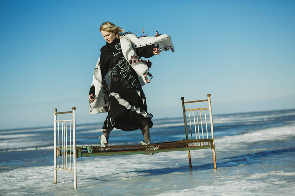 Girl in old clothes jumping on a bed on ice of frozen sea - Фото, зображення