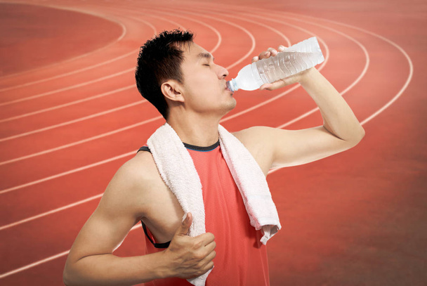 thirsty young asian handsome athlete drinking water after long run - Foto, imagen
