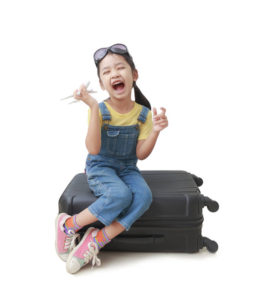 Азиатская маленькая девочка держит самолет в руке и садится на свой лагг
 - Фото, изображение