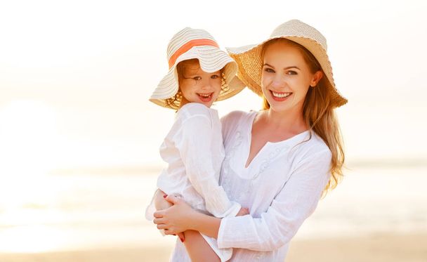 ευτυχισμένη οικογένεια στην παραλία. μητέρα και παιδί κόρη αγκαλιά στο ηλιοβασίλεμα - Φωτογραφία, εικόνα