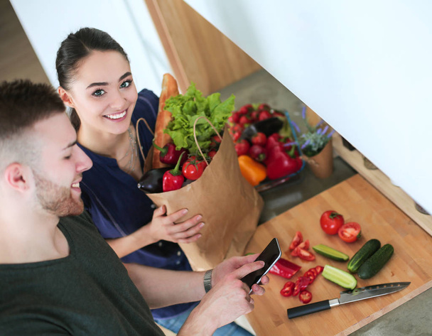 Happy couple using smartphone standing in kitchen - 写真・画像