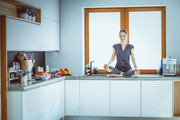 Young beautiful woman sitting at the kitchen table in the lotus position - 写真・画像