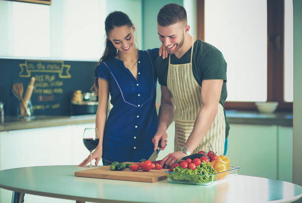 Young man cutting vegetables and woman standing with laptop in the kitchen - Foto, Imagem