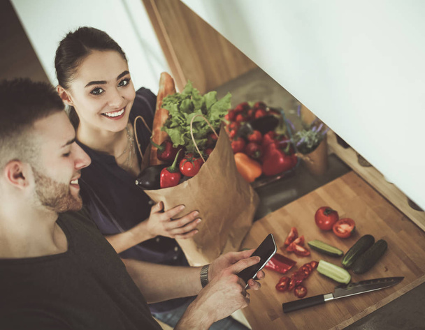 Happy couple using smartphone standing in kitchen - Foto, Bild