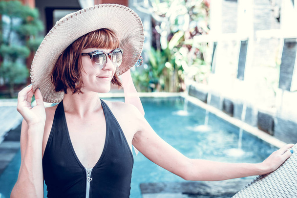 Beauty sexy woman with hat and sunglasses enjoying her summer vacation at swimming pool on a luxury villa. Summer holiday idyllic. Tropical Bali island, Indonesia. - Fotografie, Obrázek