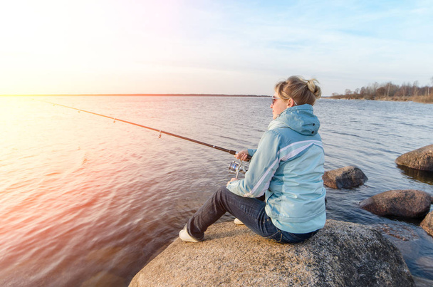 Girl sitting on a rock with a fishing rod - Photo, image