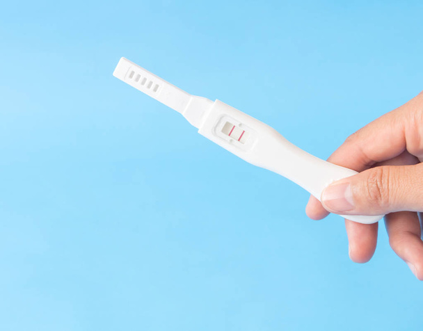 Hamilelik testi ile mavi arka plan, sağlık ve tıp kavramı tutan el - Fotoğraf, Görsel
