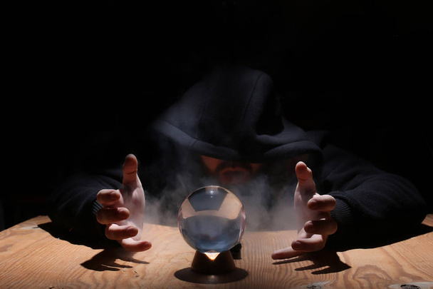hombre en una capucha negra con bola de cristal
 - Foto, Imagen