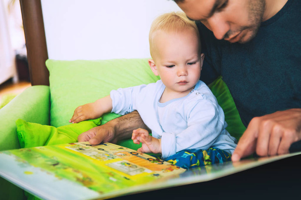 A little boy is reading a book with his father in a home interio - Foto, imagen