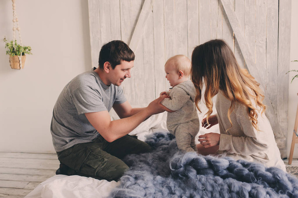 happy family playing at home on the bed. Lifestyle capture of mother, father and baby in modern scandinavian interior - Zdjęcie, obraz
