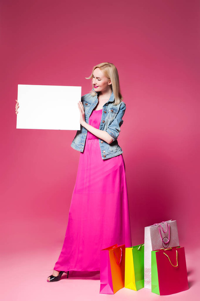 Shopping woman holding shopping bags on pink background . Holds a white nameplate for your text - 写真・画像
