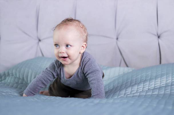 Wily faced baby boy sitting on the bed. Infant kid in playful mood. Happy toddler playing indoor - Zdjęcie, obraz