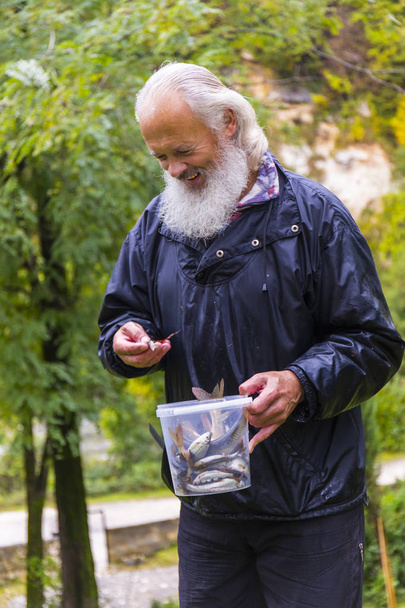 Positive gray-haired fisherman with his small catch - Zdjęcie, obraz