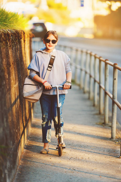 glückliches 9-jähriges Schulmädchen mit Rucksack in den Straßen der Stadt, mit Roller, Sonnenbrille - Foto, Bild