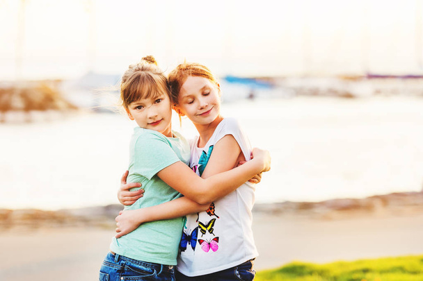 zwei 9-10 jährige Mädchen spielen zusammen draußen, umarmen sich, goldene Stunde - Foto, Bild