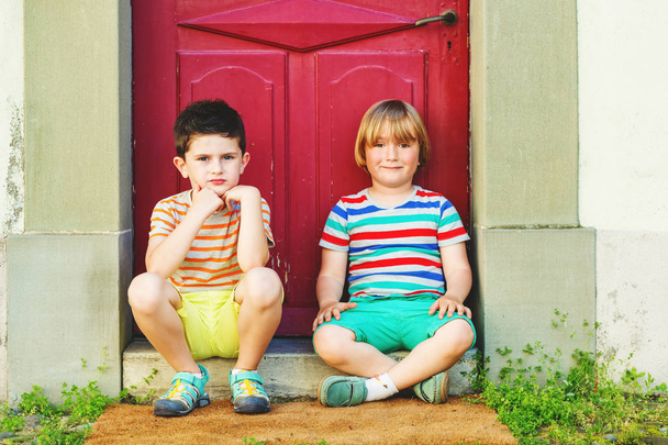 Grupo de dos niños divertidos jugando juntos al aire libre, con camisetas de colores, pantalones cortos y zapatos, moda de verano para niños
.  - Foto, imagen