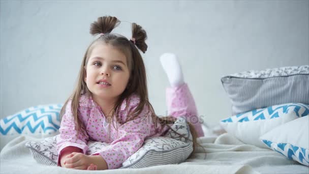 Dziewczynka w ładny piżamy na łóżko i starannie drżenie nogi - Materiał filmowy, wideo