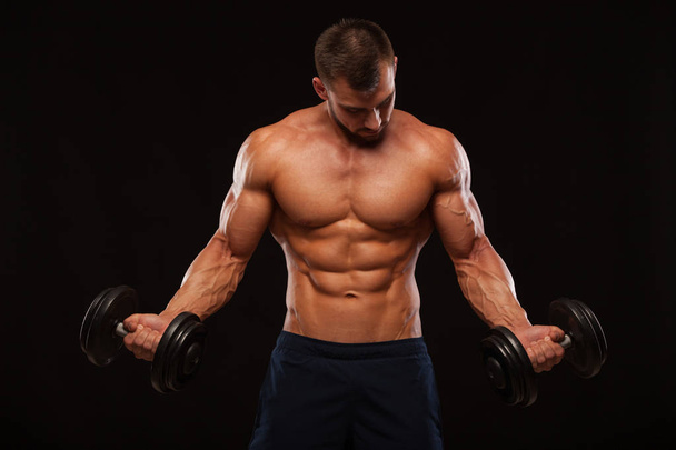 muskulöser, gutaussehender Mann trainiert im Fitnessstudio mit Kurzhanteln. isoliert auf schwarzem Hintergrund mit Copyspace - Foto, Bild