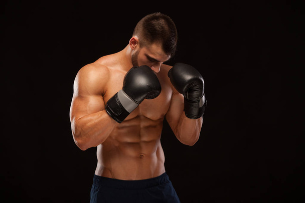 Muscular young man with perfect Torso with six pack abs, in boxing gloves is showing the different movements and strikes isolated on black background with copyspace - Foto, afbeelding
