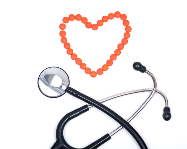Апельсиновые таблетки в форме сердца и черный кардиологический стетоскоп
 - Фото, изображение