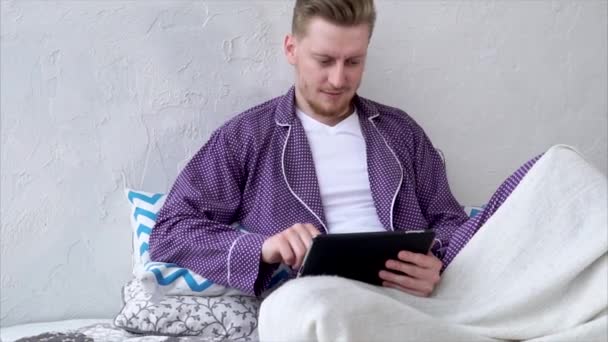 Молодий чоловік у піжамі грає на портативні таблетку в ігри через Інтернет - Кадри, відео